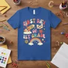Retro "First Day of 1st Grade" text with rocket, book, apple, and rainbow graphics on a blue t-shirt